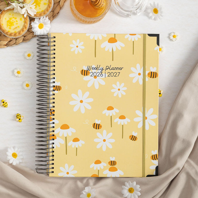 Weekly planner with floral design on a light surface with a straw hat and flowers.
