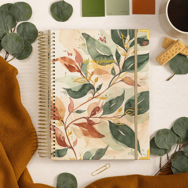 Notebook with leaf design on a white surface with coffee and greenery