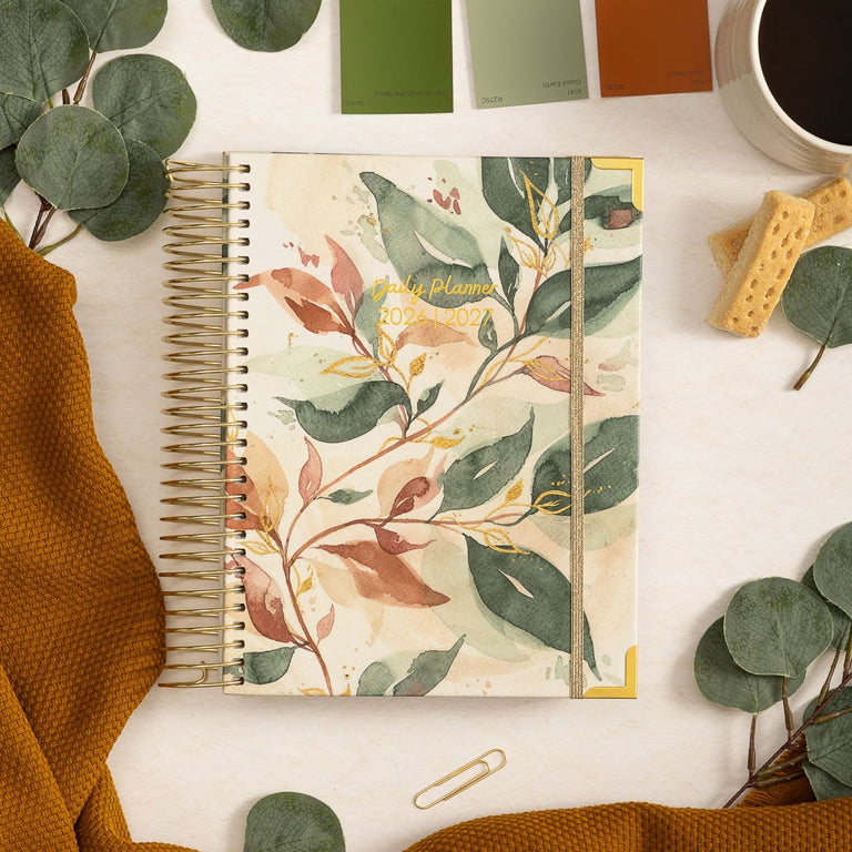 Notebook with floral design, coffee cup, and eucalyptus leaves on a white surface