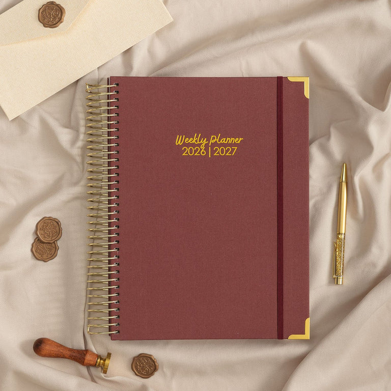 Maroon planner with gold accents on a beige fabric background