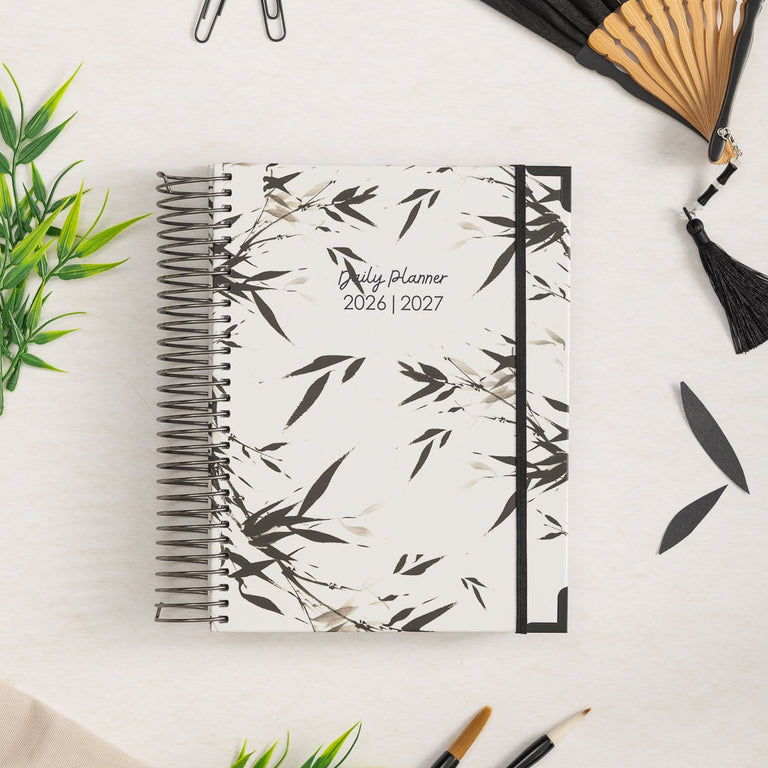 Planner with bamboo design, black fan, and stationery items on a light background