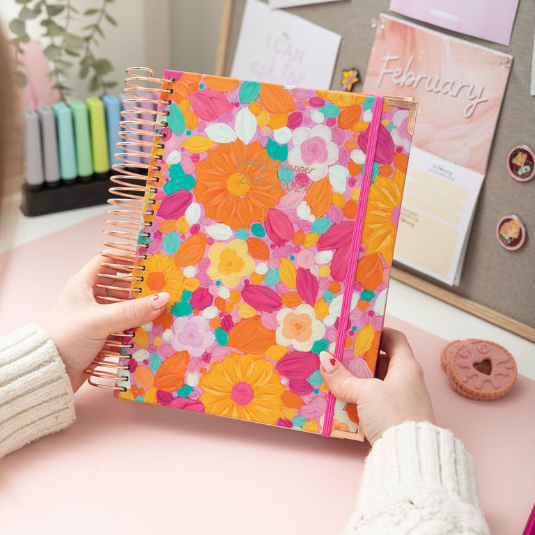 Person holding a colorful floral notebook with a desk and calendar in the background