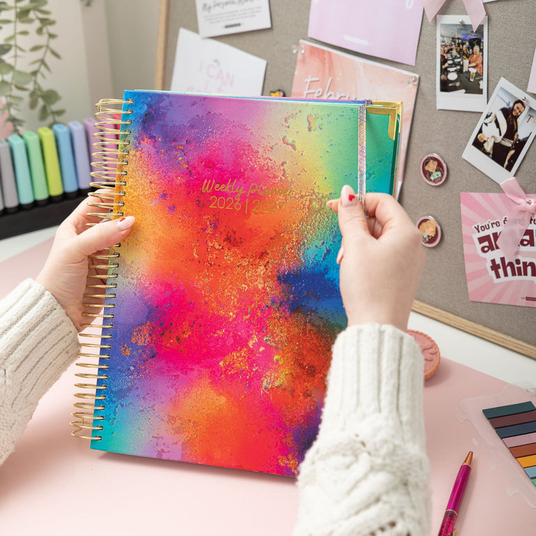 Person holding a colorful planner with a decorated wall in the background