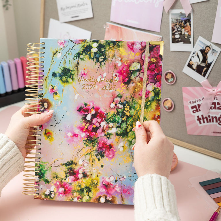 Person holding a floral notebook with a decorated wall in the background