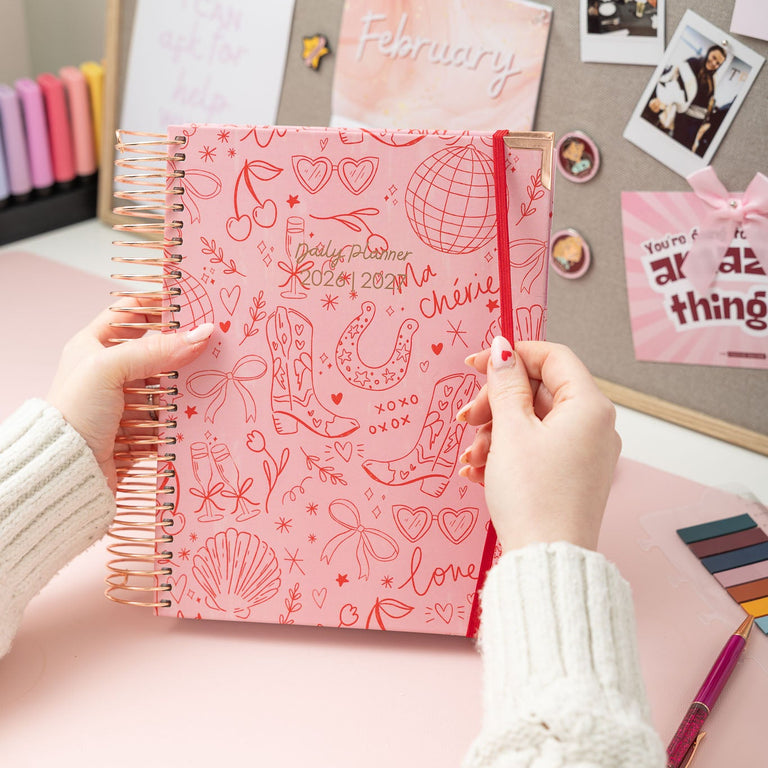 Person holding a pink notebook with decorative cover against a desk background