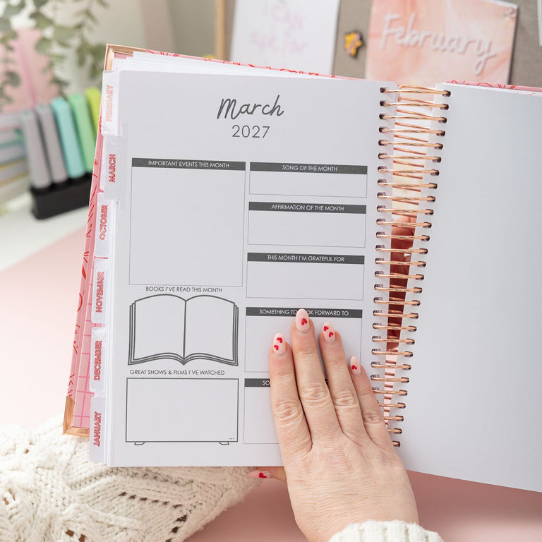 Person holding a planner open to March 2027 with a pink background