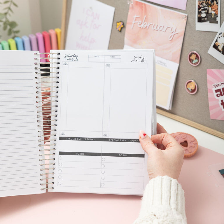 Person holding a planner next to a decorative wall with photos and notes.