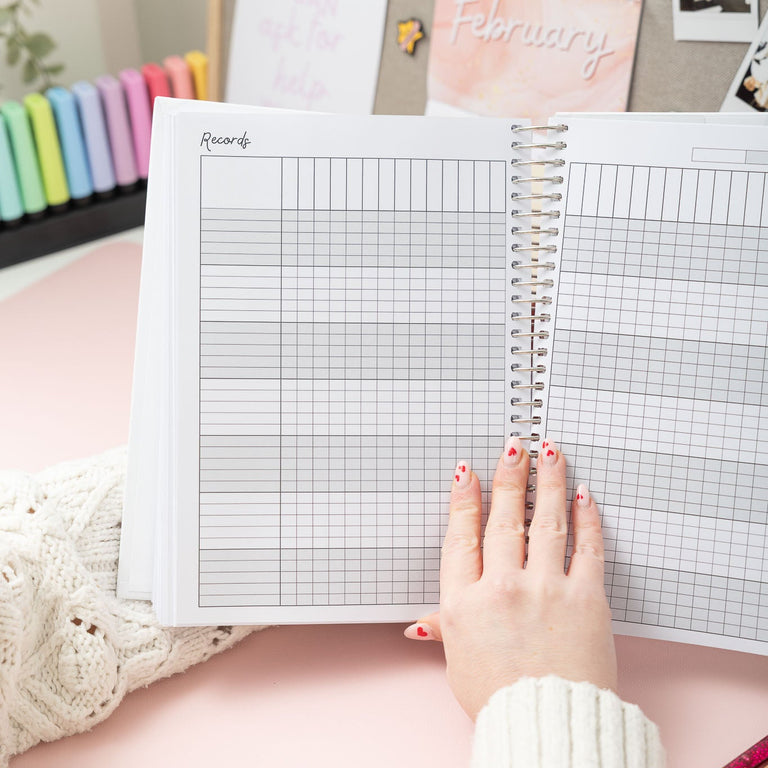 Person holding an open notebook with grid paper on a desk with stationery items.