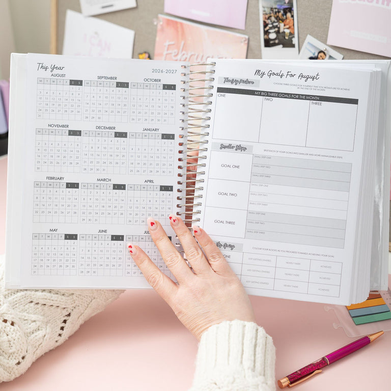 Person holding a planner with a pink background and decorative elements