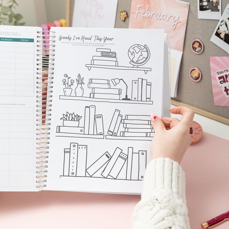 Person holding a planner with a design of books on a desk with stationery items.