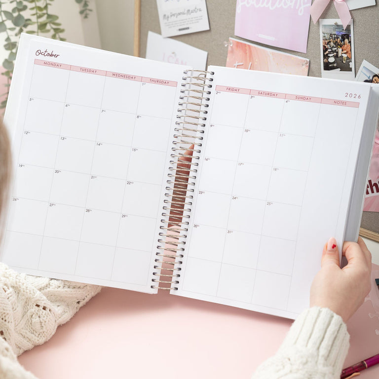 Person holding a spiral-bound planner with decorative elements in the background
