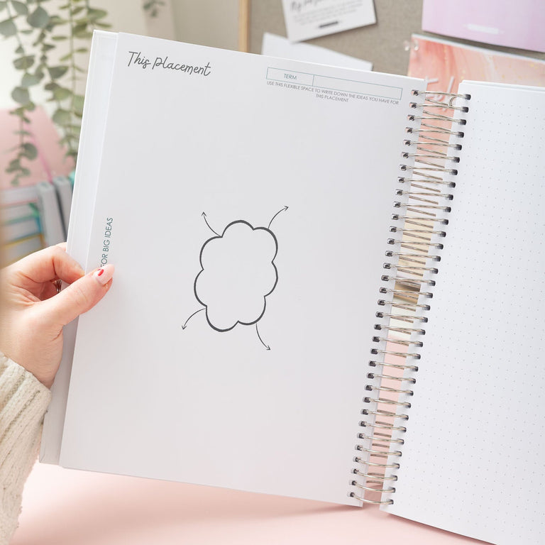 Person holding a spiral-bound notebook with a cloud drawing on a desk.