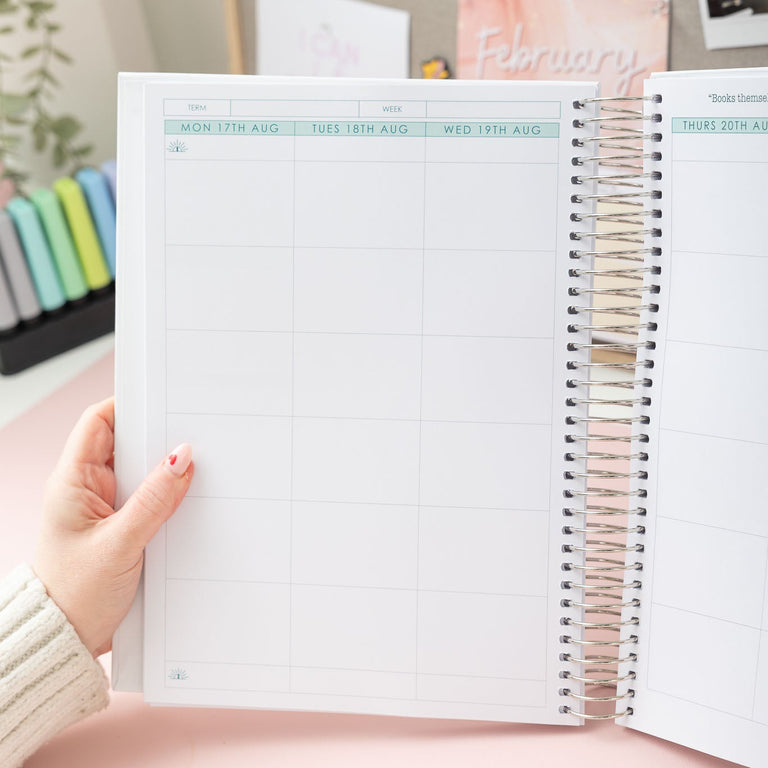 Person holding a spiral-bound notebook with a pink cover and white pages.