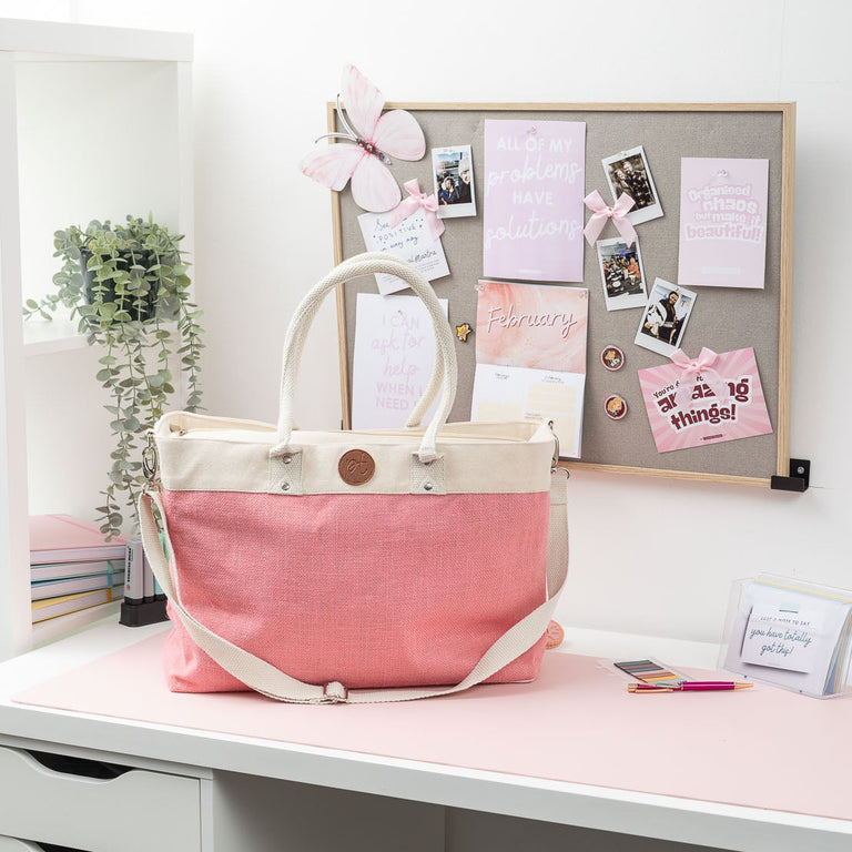 White desk with a pink tote bag, drawers, and a bulletin board with notes and photos.