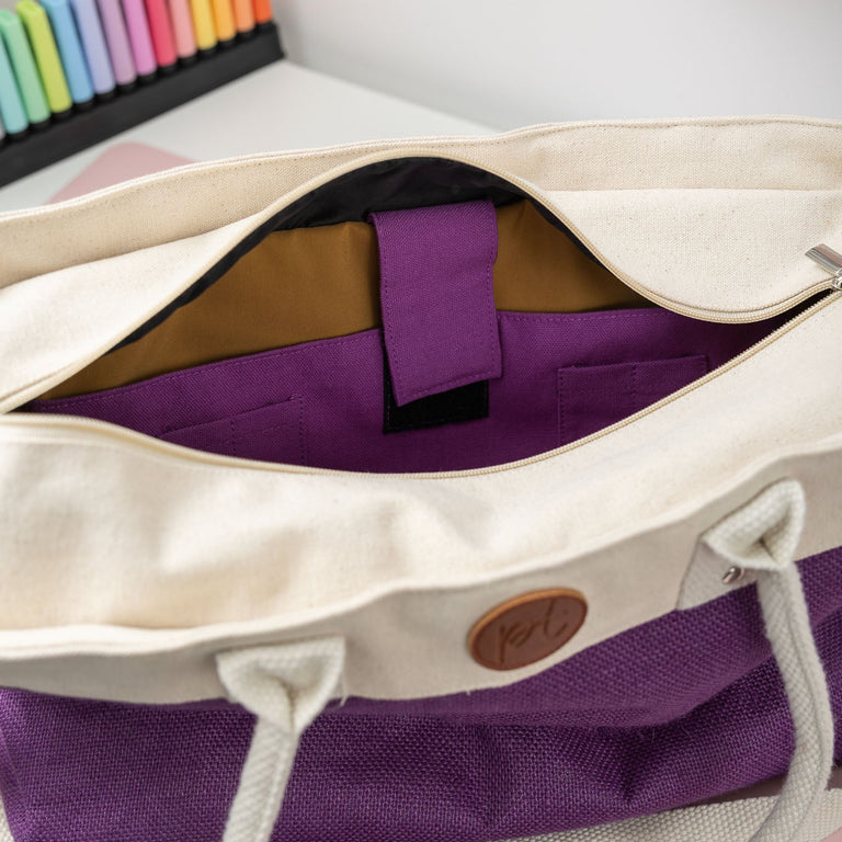 White tote bag with purple interior and handle on a desk.