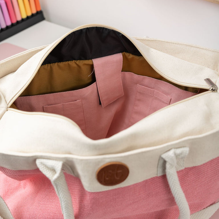 Open beige bag with pink garment inside, on a light pink surface.