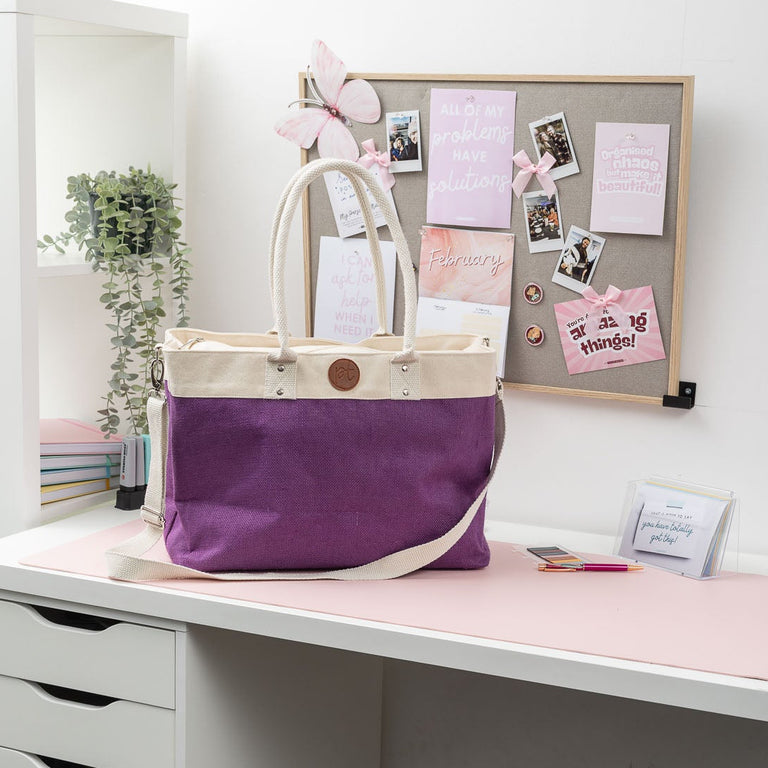 Purple tote bag on a white desk with a bulletin board in the background