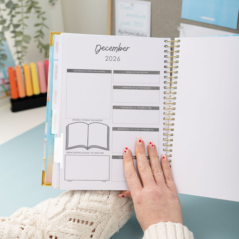 Person holding a planner open to December 2024 on a light blue surface.