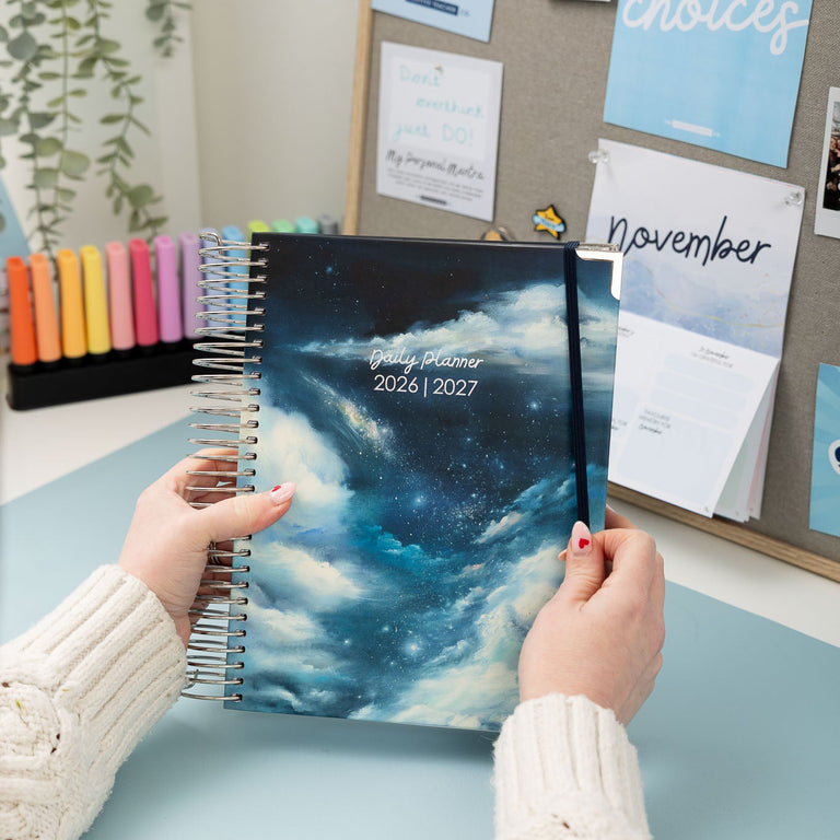 Person holding a spiral-bound planner with a celestial design on a desk.