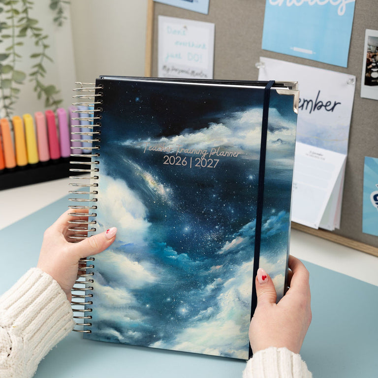 Person holding a planner with a cosmic design on a desk with office supplies in the background