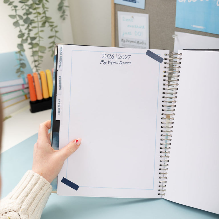 Person holding a spiral-bound planner with a home office background