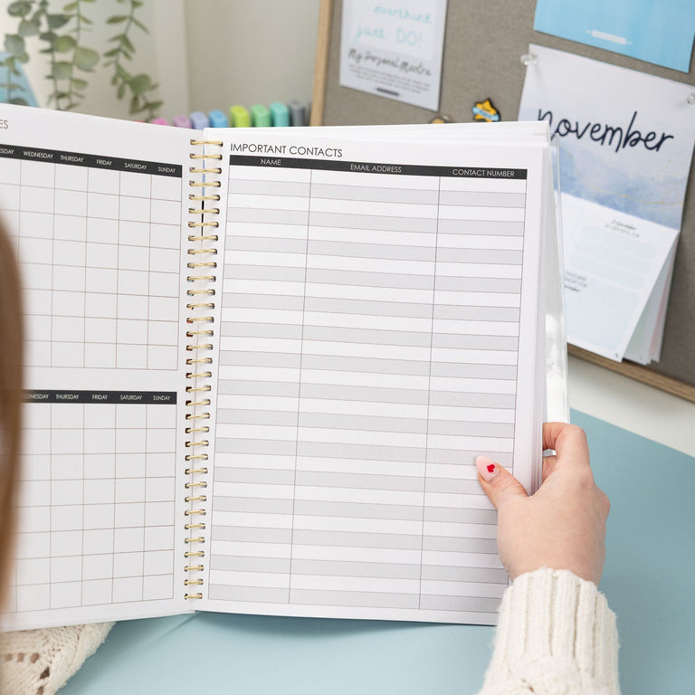 Person holding an open planner with a desk and wall decorations in the background