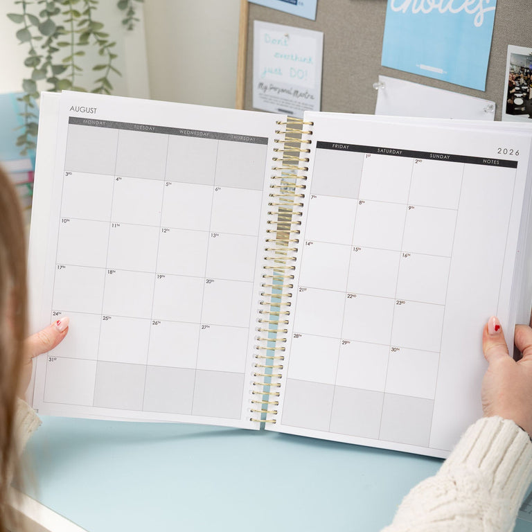 Person holding a large spiral-bound planner with a calendar on a light blue surface.