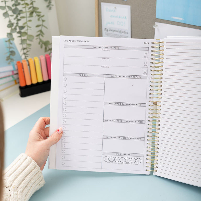Person holding an open planner with a desk and decor in the background