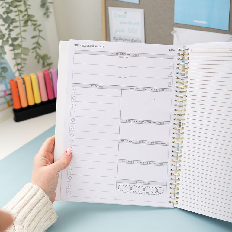 Person holding an open planner with a light blue desk and motivational posters in the background