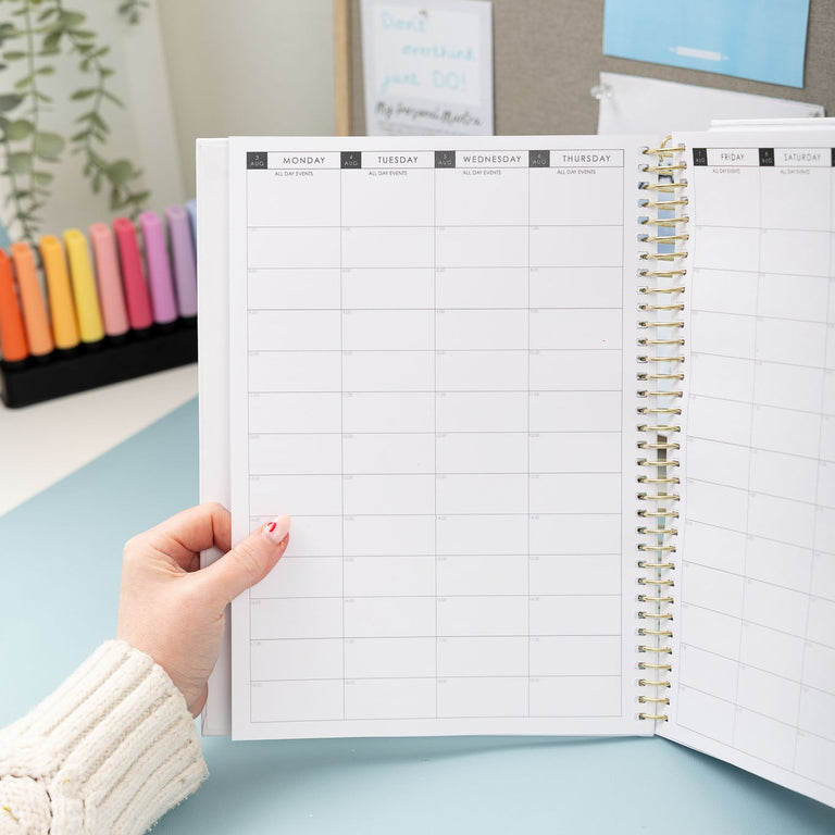Person holding an open planner with a grid layout on a light blue surface.