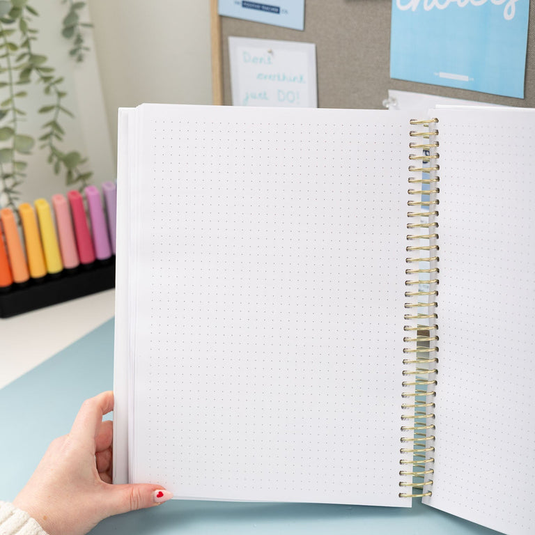 Person holding a spiral-bound notebook with motivational posters in the background
