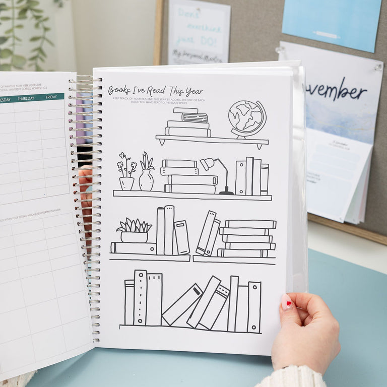 Person holding a planner with a bookshelf illustration on a desk with a calendar in the background