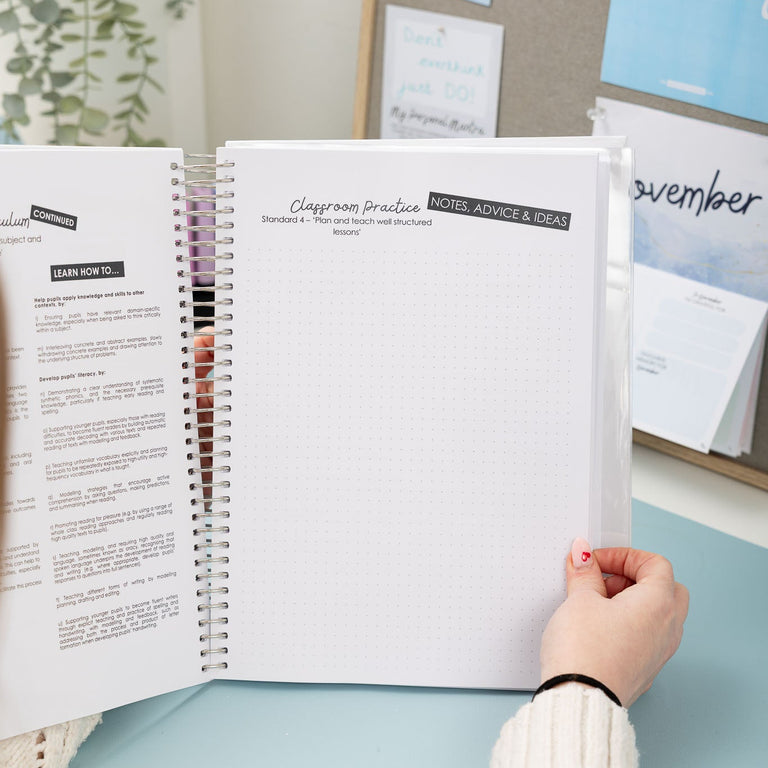 Person holding an open planner with a desk and wall with notes in the background