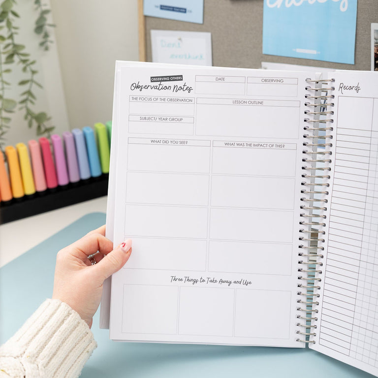 Person holding an open planner with a visible page, set against a background with colorful markers and motivational posters.