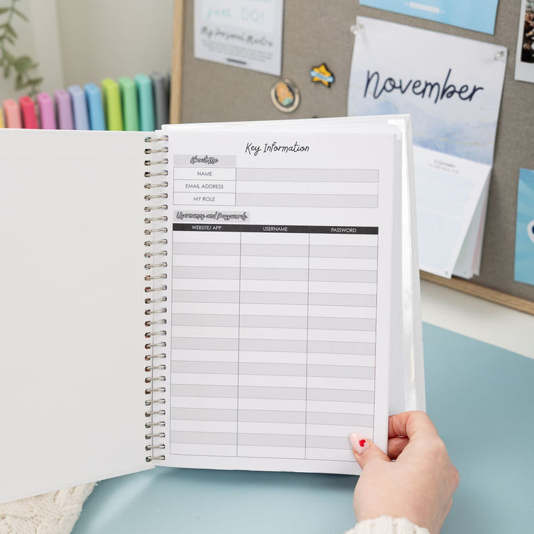 Person holding a planner with a budgeting sheet in front of a bulletin board with notes and photos.