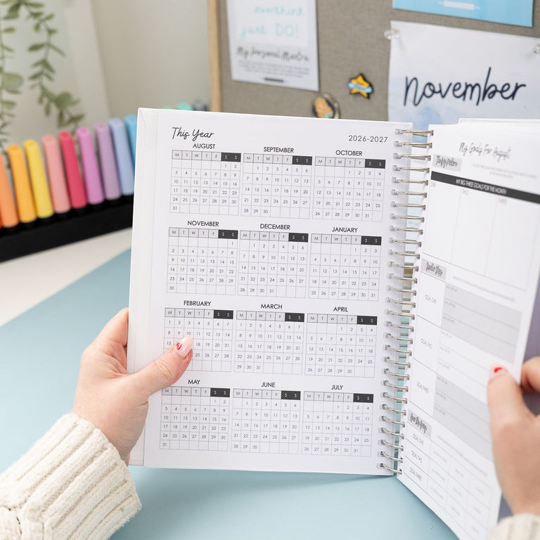 Person holding a planner with a calendar view on a light blue surface.