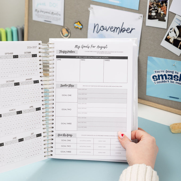 Person holding a planner with a calendar on a desk with various items in the background