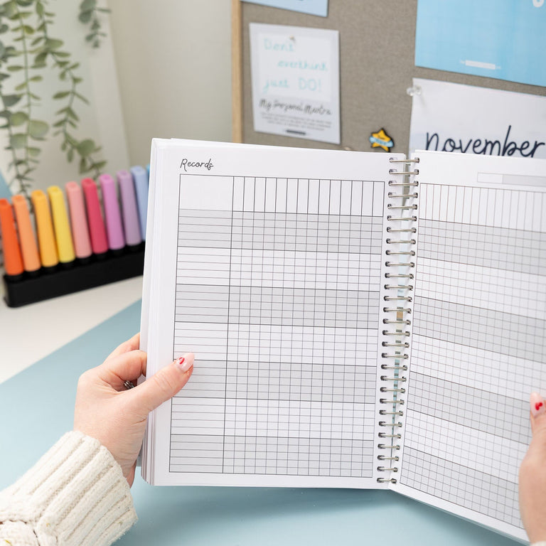 Person holding a planner with grid and monthly layout on a light blue surface.