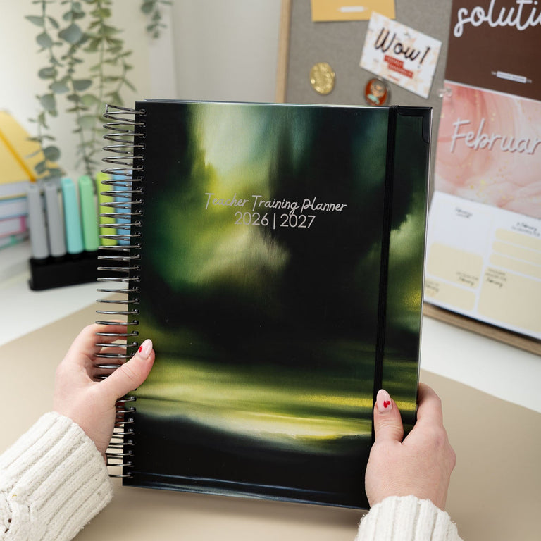 Person holding a planner with a blurred background of a desk and office items.
