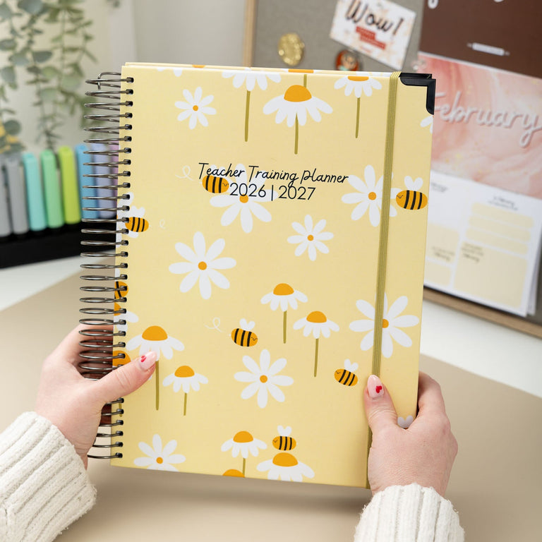 Person holding a yellow planner with floral design and text on a desk.