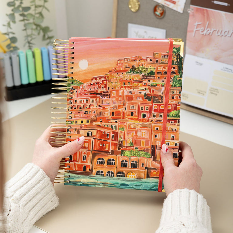 Person holding a colorful notebook with a scenic cover in an office setting.