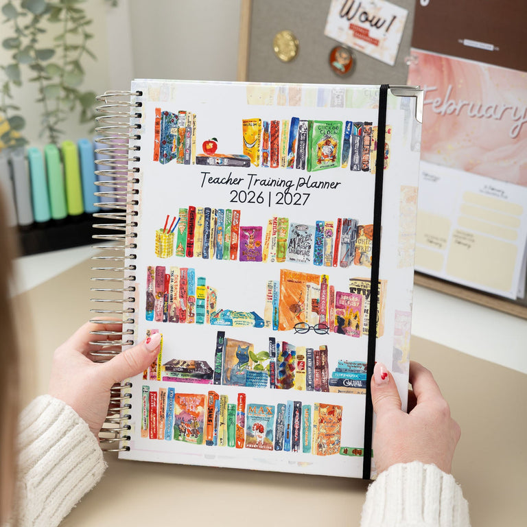 Person holding a colorful planner with a classroom theme on a desk.