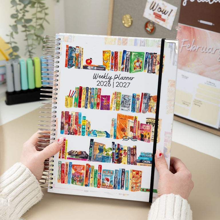 Person holding a colorful weekly planner on a desk with office supplies in the background