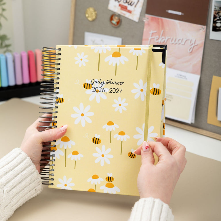 Person holding a yellow planner with floral design in an office setting