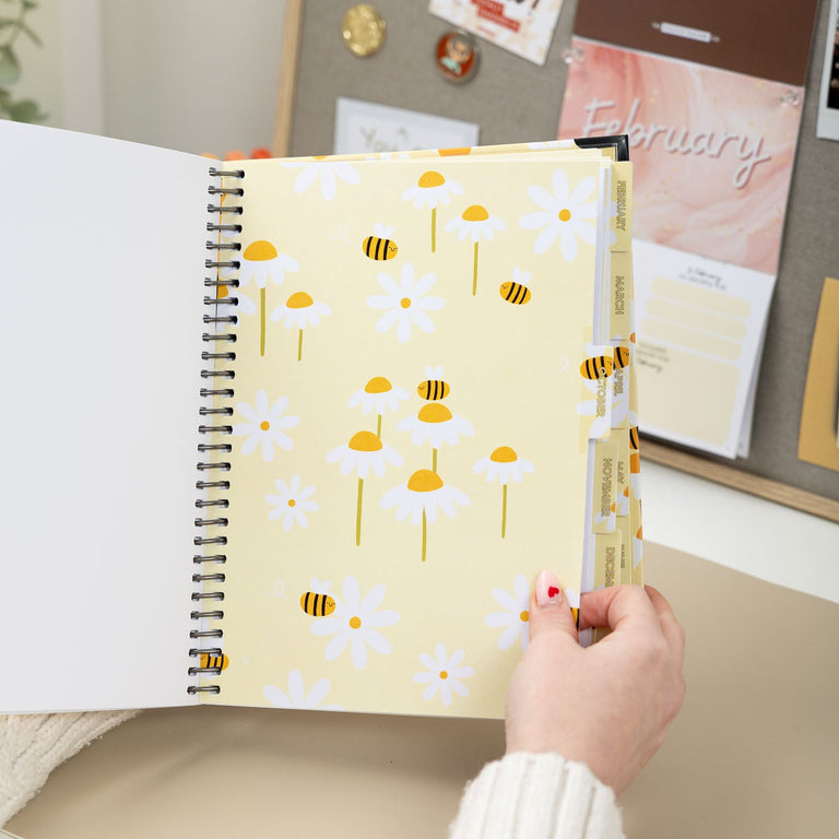 Person holding a spiral-bound notebook with floral design on a desk.