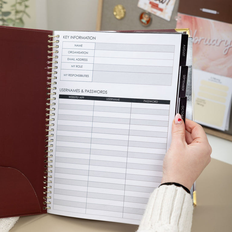 Person holding a planner with a password management section on a desk.
