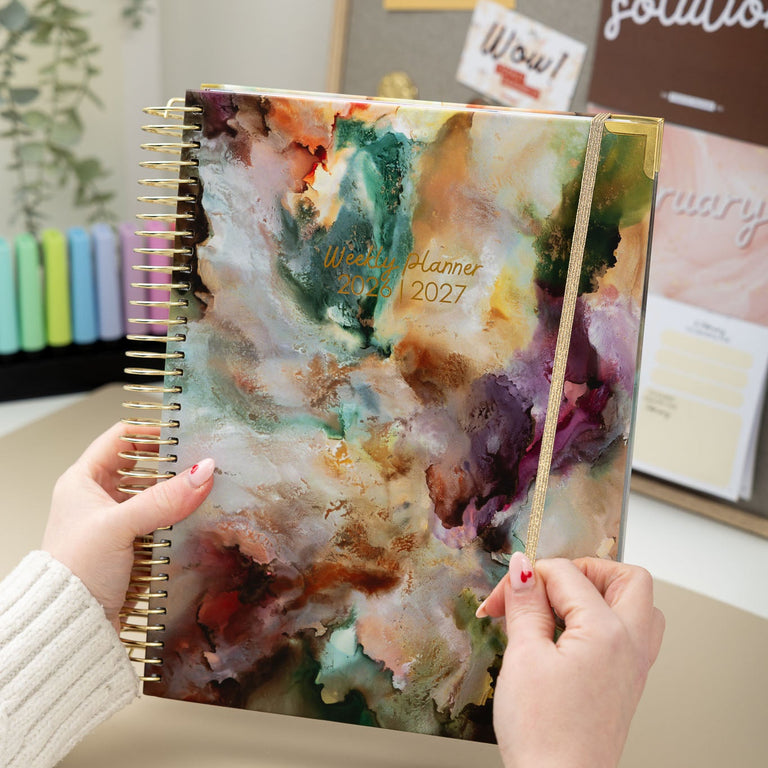 Person holding a planner with a colorful abstract design in an office setting.