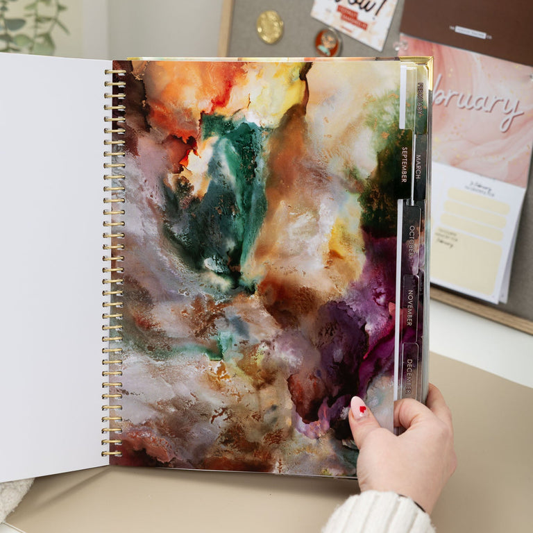Person holding a planner with a colorful abstract design on a desk.
