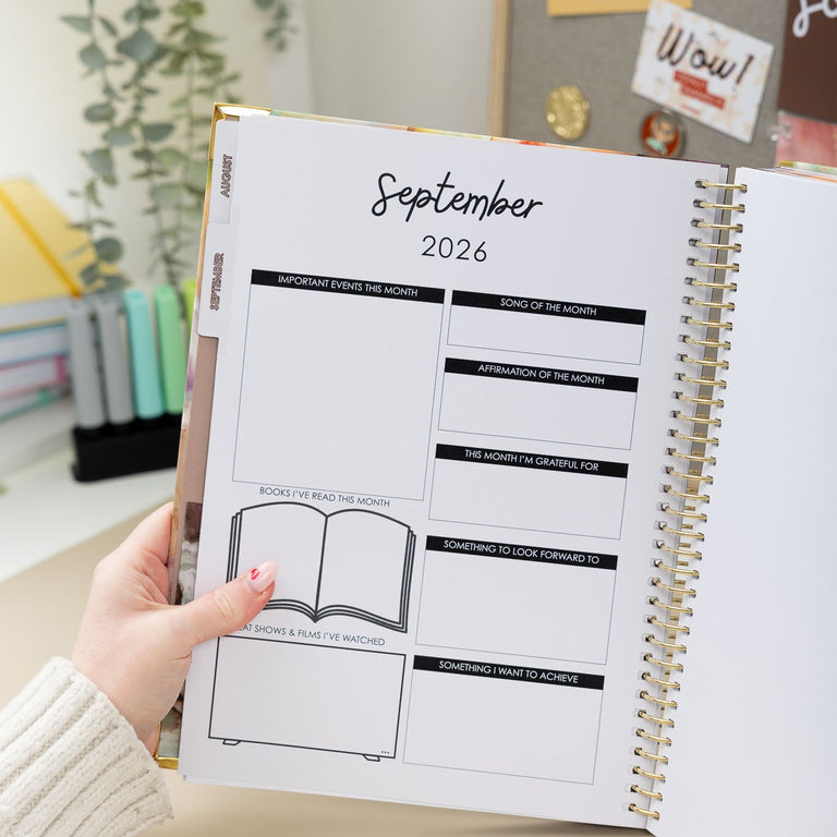 Person holding a planner open to September 2026 with a home office background.