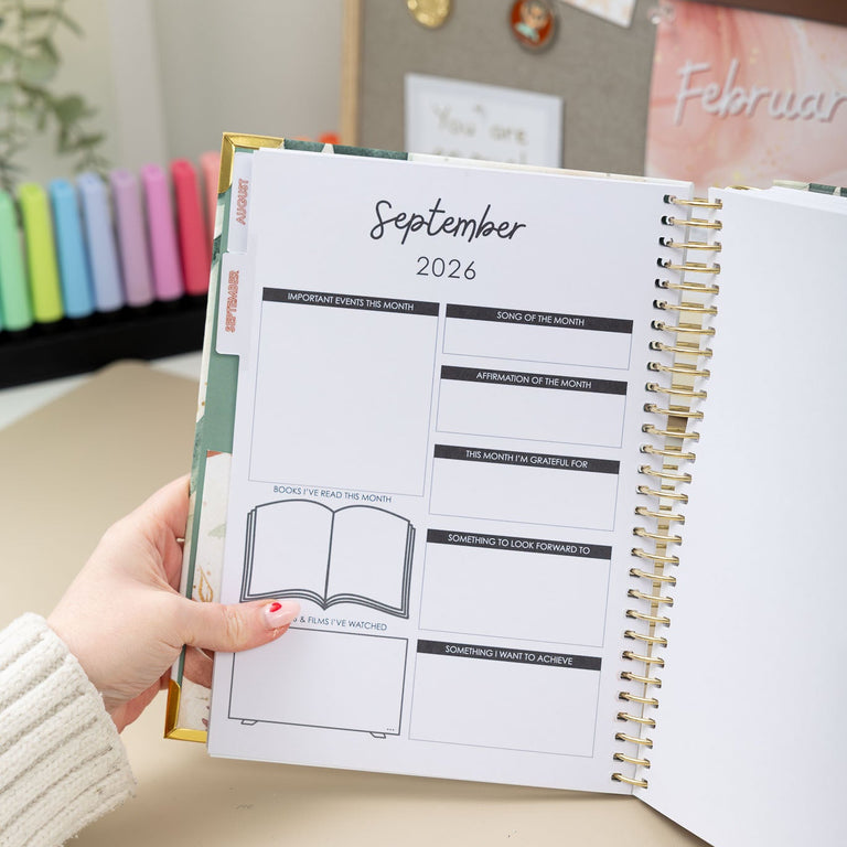Person holding a planner open to September 2026 on a desk with office supplies in the background.